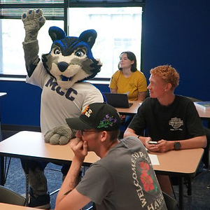 MCC Wolf raising hand sitting next to student