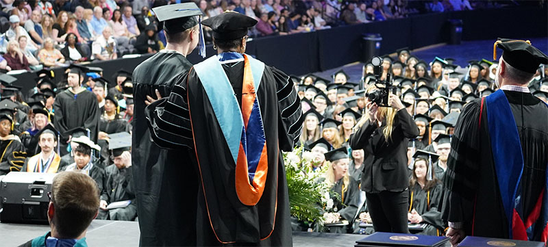 2023 Commencement Recap - A new grad crossing the commencement stage pauses for a photo with the chancellor.